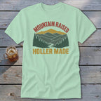 Light green t-shirt featuring a retro mountain landscape graphic and the text Mountain Raised Holler Made.