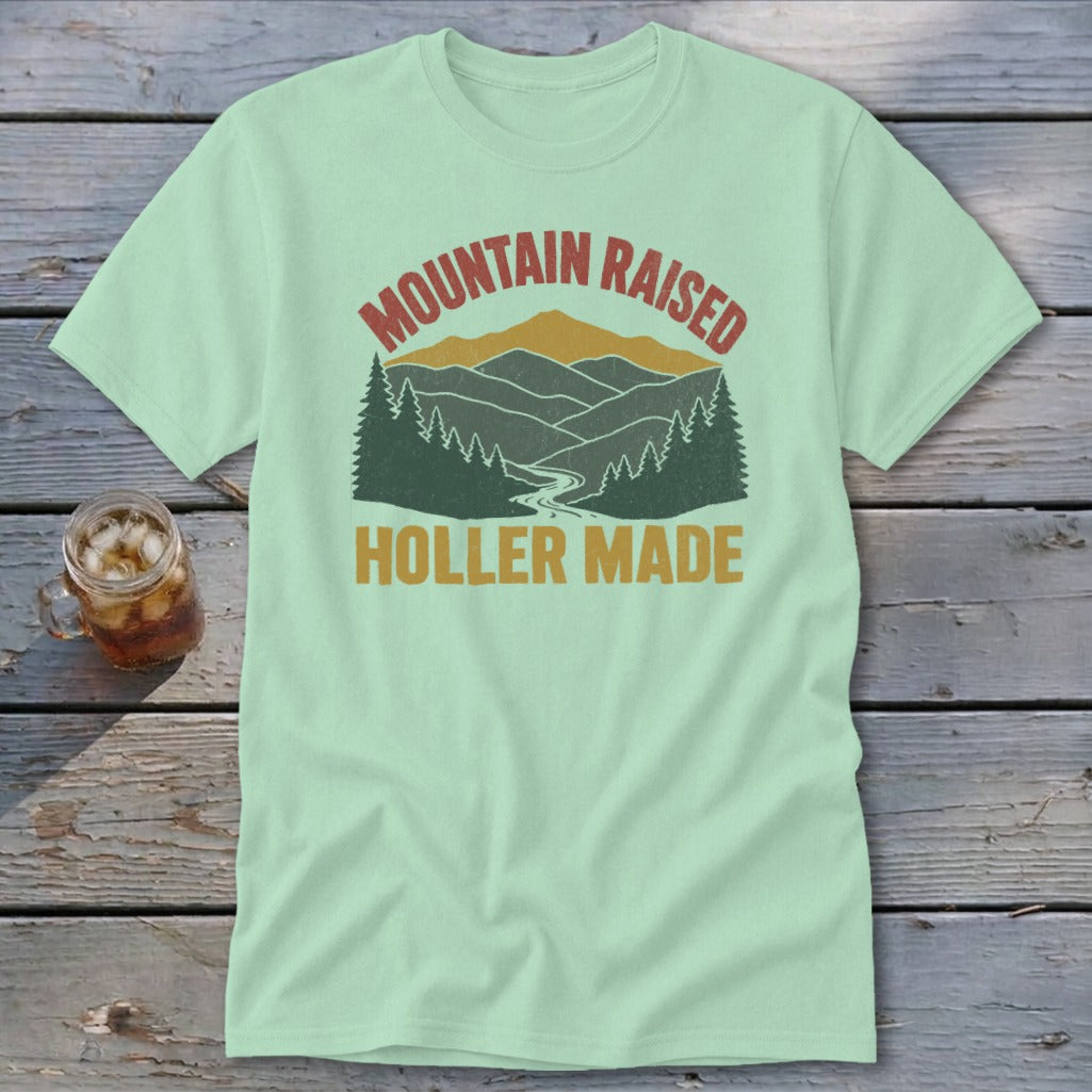 Light green t-shirt featuring a retro mountain landscape graphic and the text Mountain Raised Holler Made.
