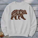 A white crewneck sweatshirt featuring a brown graphic of a walking bear containing the word Appalachia.