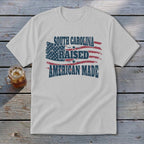 White t-shirt with "South Carolina Raised American Made" text over distressed US flag.
