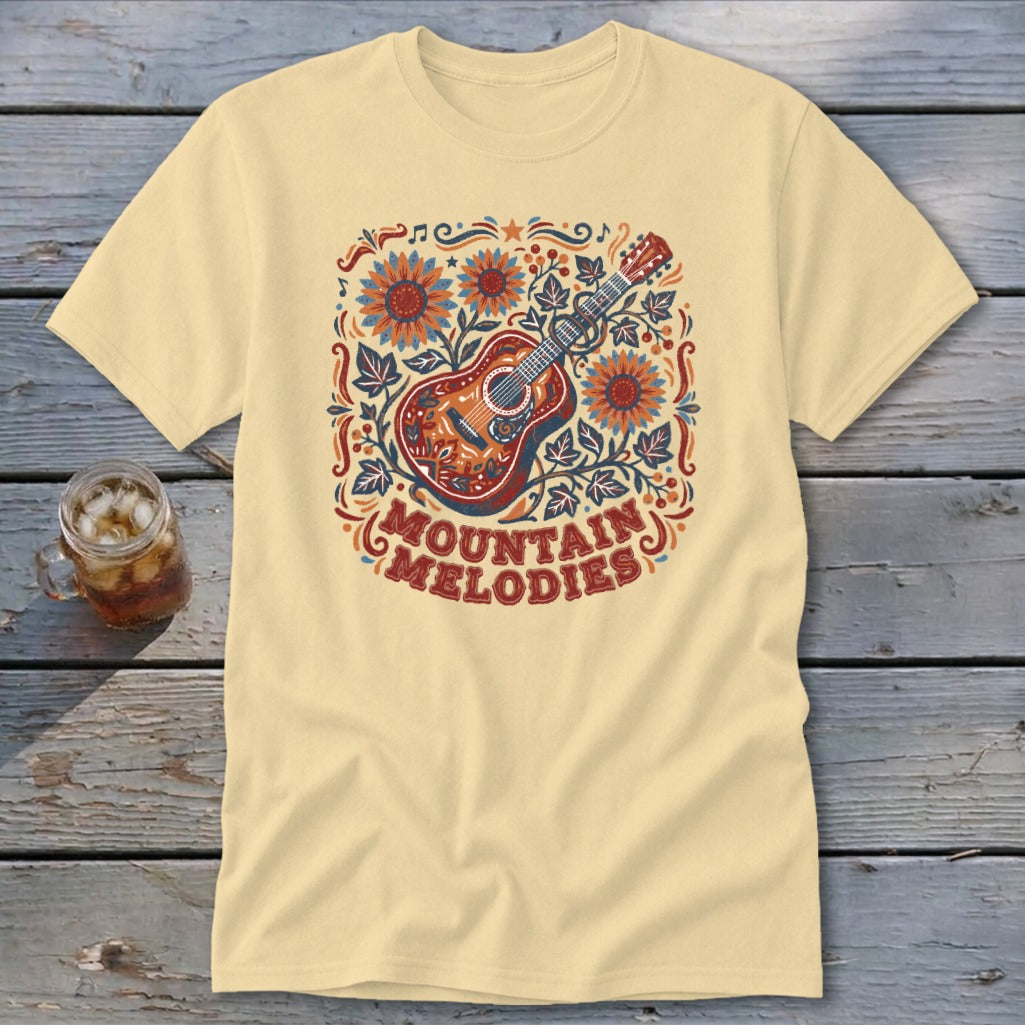 A light yellow t-shirt with a vintage-style graphic of a guitar, sunflowers, leaves, and the text "Mountain Melodies".