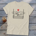 Cream t-shirt with line drawing of couple and dog on a swing with mountains and red heart.