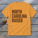 Orange t-shirt with brown text reading "NORTH CAROLINA RAISED".