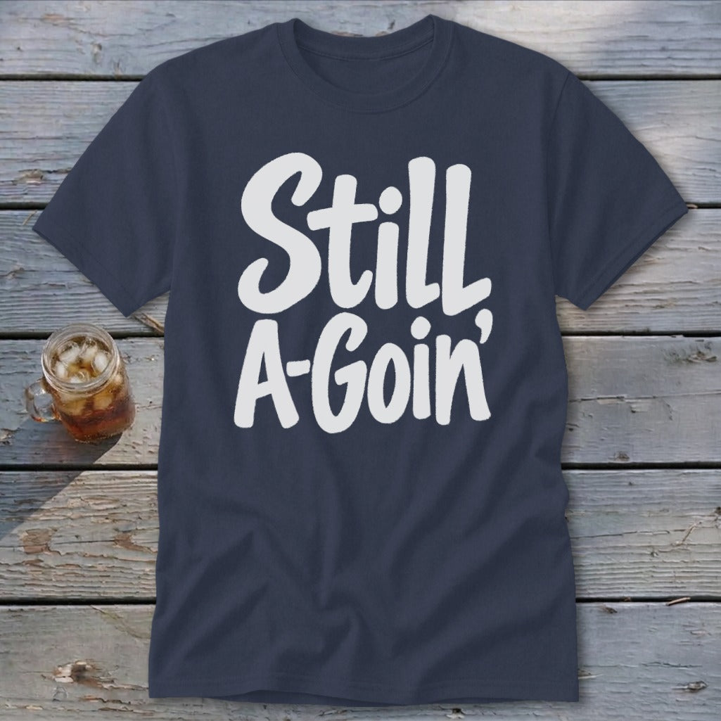 Dark blue t-shirt featuring the white text Still A-Goin' laid flat on wooden planks.