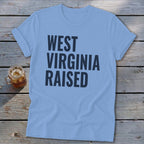 Light blue t-shirt with bold dark blue text "WEST VIRGINIA RAISED".