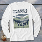 A white long-sleeved t-shirt featuring a Blue Ridge Parkway graphic with mountains, a winding road, and evergreen trees.