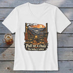 White t-shirt with a graphic of rocking chairs on a porch and the text "Pull up a chair The holler's talkin'".