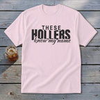 Pink t-shirt with black text "THESE HOLLERS know my name" and a glass of iced tea.