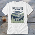 A white t-shirt featuring a Blue Ridge Parkway graphic with mountains, trees, and a winding road.