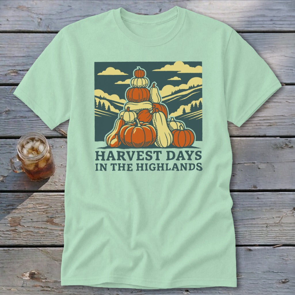 Light green t-shirt with a graphic of stacked pumpkins, hills, and the text Harvest Days in the Highlands.