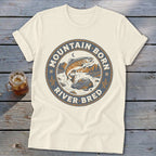 Cream t-shirt with a circular graphic featuring a leaping trout, river, and mountains. Text reads "Mountain Born River Bred".