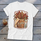 White t-shirt with sorghum stalks in a wooden barrel, featuring the word "Sorghum".