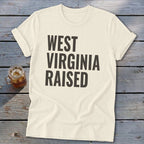 Cream t-shirt with "WEST VIRGINIA RAISED" printed in dark grey block letters.