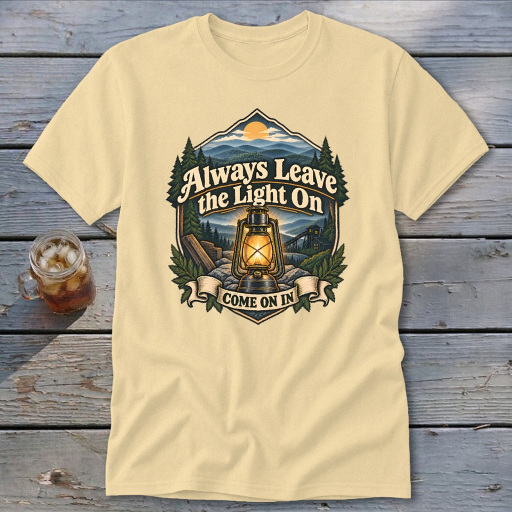 Light yellow t-shirt with graphic of lantern, mountains, and text "Always Leave the Light On Come On In".