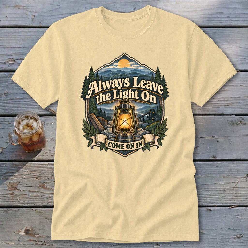 Light yellow t-shirt with graphic of lantern, mountains, and text "Always Leave the Light On Come On In".
