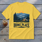 A yellow t-shirt with a landscape graphic of a cabin in the mountains and text reading THE HOME PLACE.
