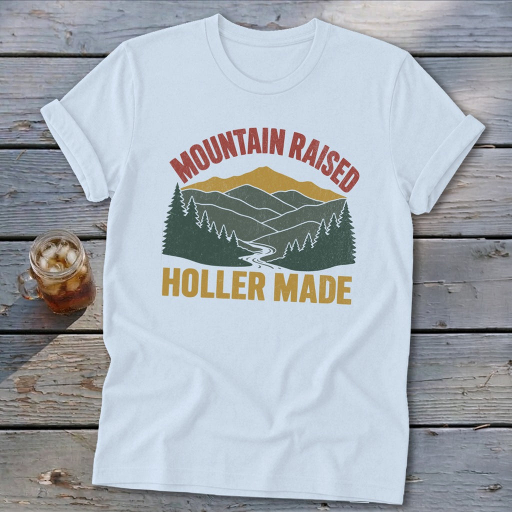 White t-shirt with a vintage mountain landscape graphic and the text Mountain Raised Holler Made.