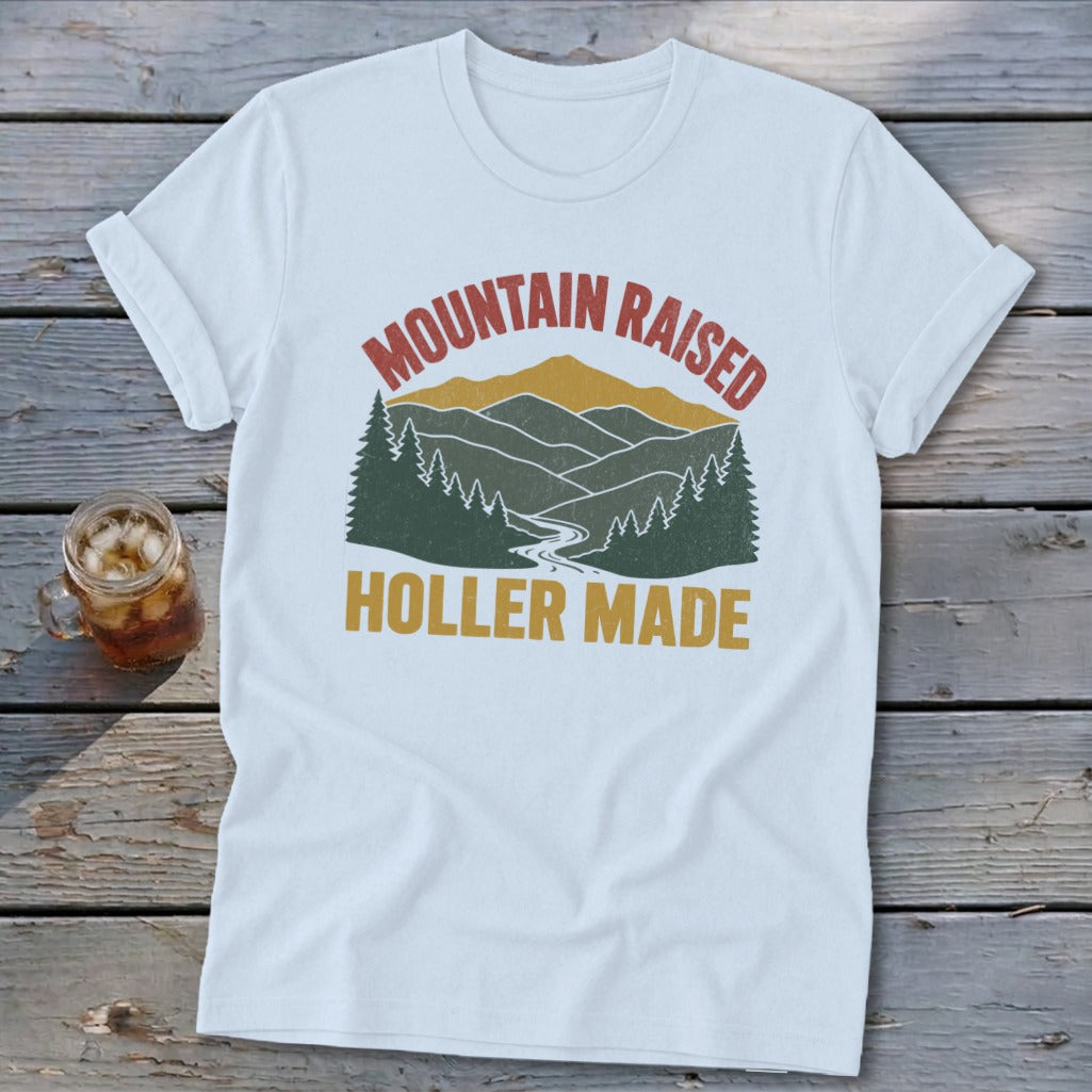 White t-shirt with a vintage mountain landscape graphic and the text Mountain Raised Holler Made.