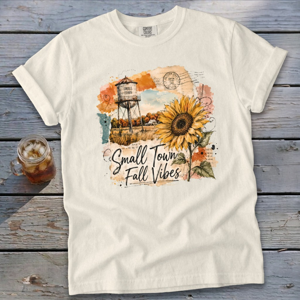 Cream t-shirt with a graphic of a water tower, sunflower, and "Small Town Fall Vibes" text.