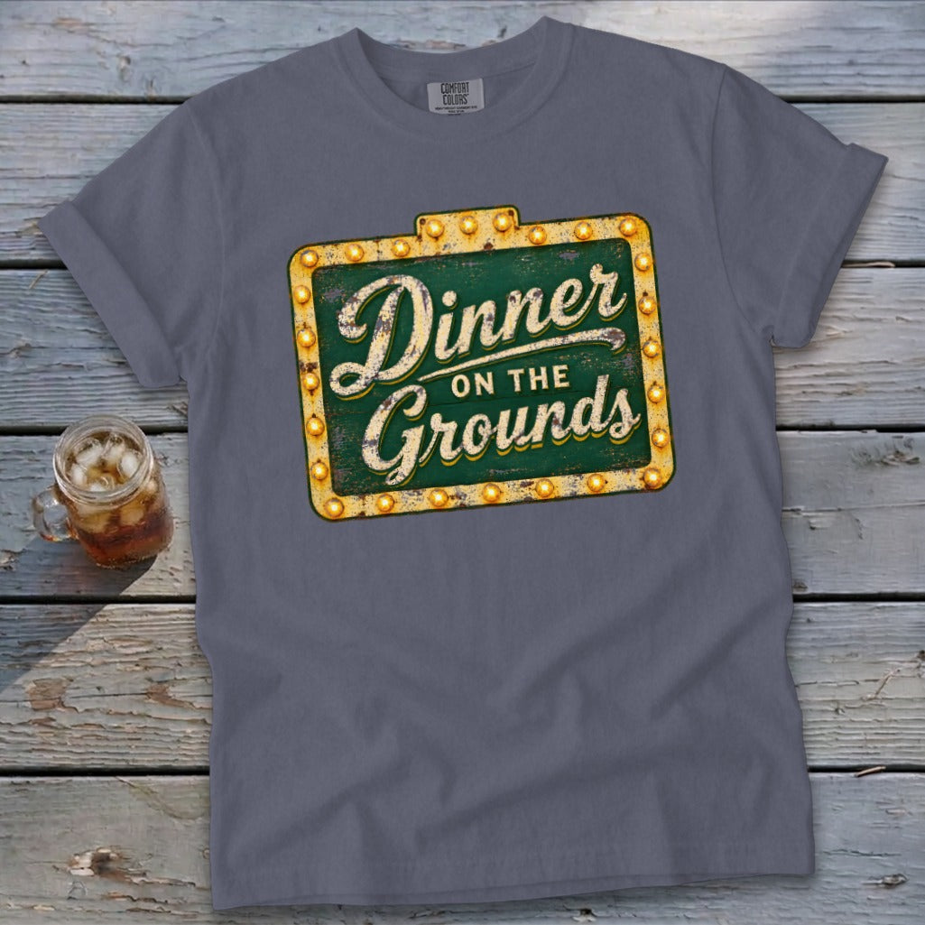 A slate grey t-shirt featuring a green sign graphic with the text "Dinner on the Grounds".