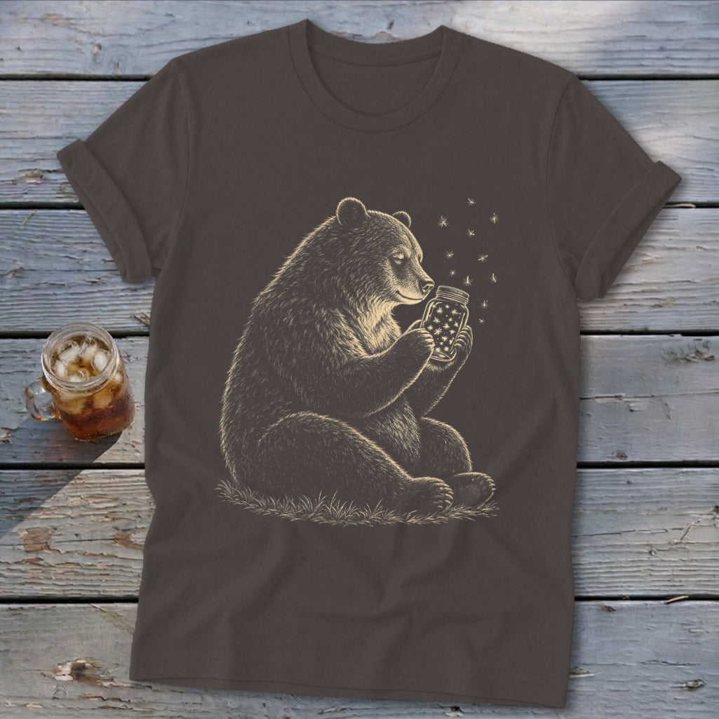 Bear holding a jar filled with stars and fireflies on a dark brown t-shirt.