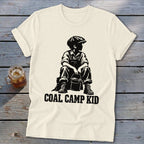 Cream t-shirt with black graphic of a boy sitting and holding a bucket, text "COAL CAMP KID".