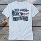 White t-shirt with distressed American flag design and text: South Carolina Raised American Made.