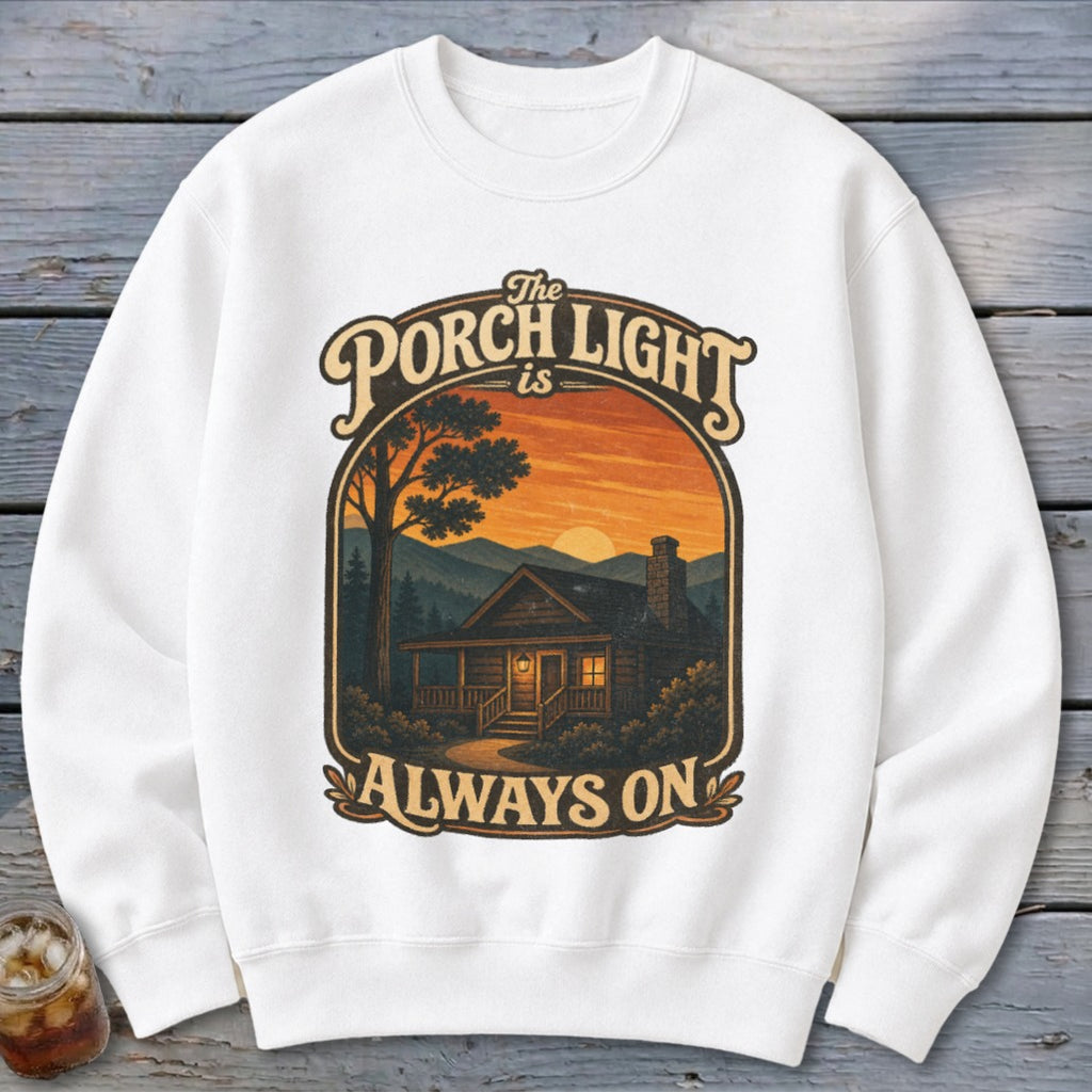 White sweatshirt with graphic: "The Porch Light is Always On" above a log cabin at sunset.