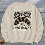 Beige crewneck sweatshirt featuring a graphic of a woolly worm caterpillar with text reading Woolly Worm Winter Prophet.