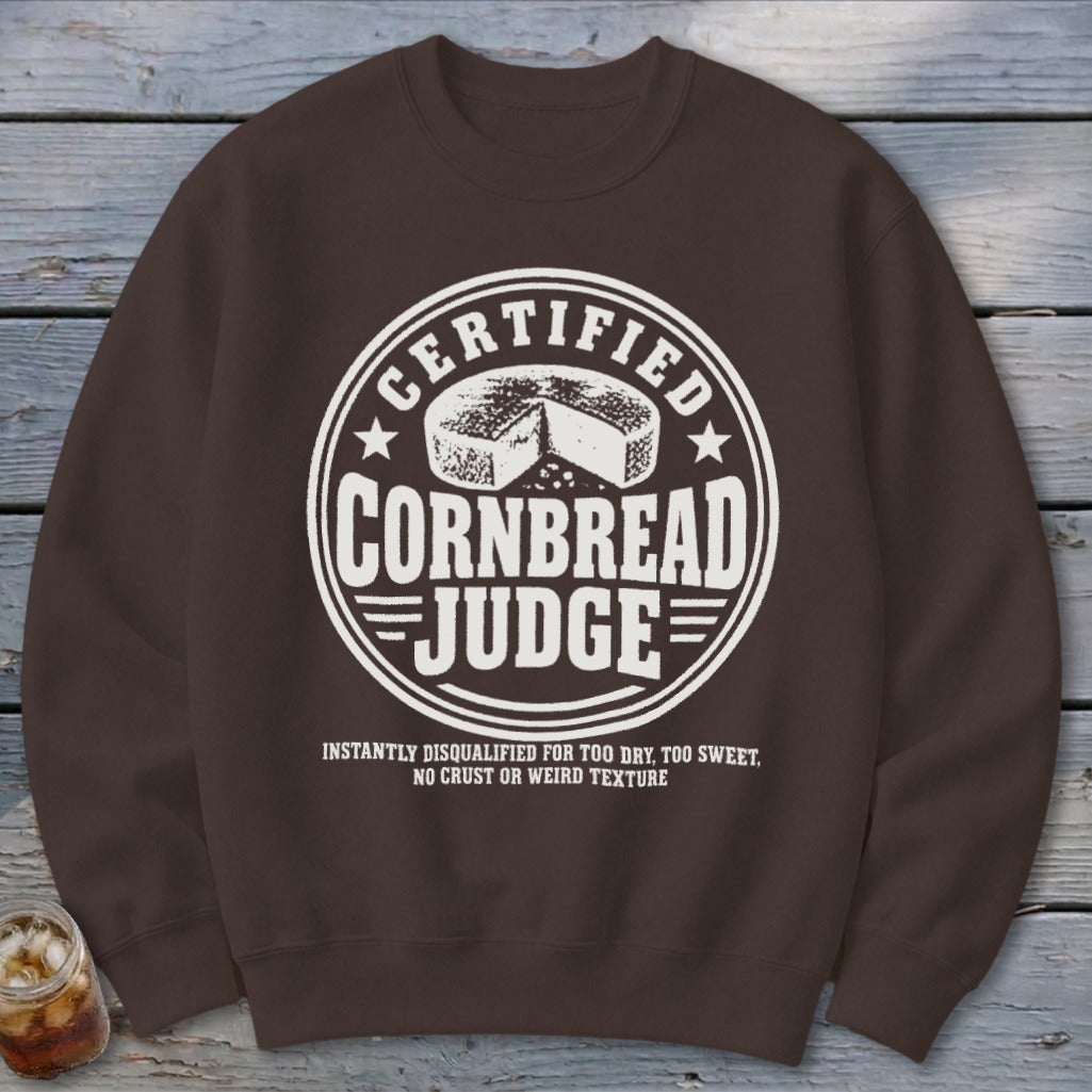 A dark brown crewneck sweatshirt featuring a white circular graphic that reads "Certified Cornbread Judge".
