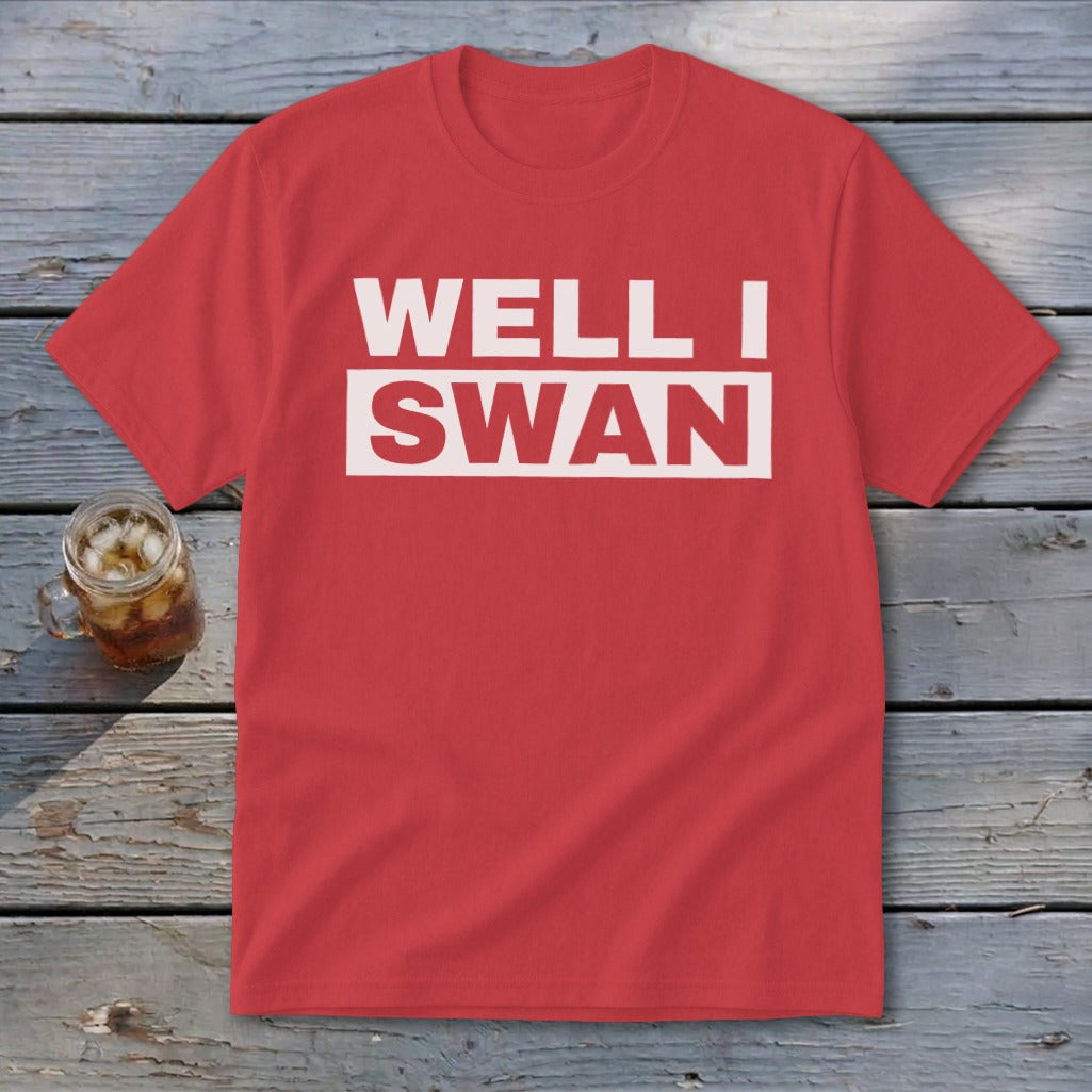 Red t-shirt featuring the white text WELL I SWAN lying flat on a wooden surface.
