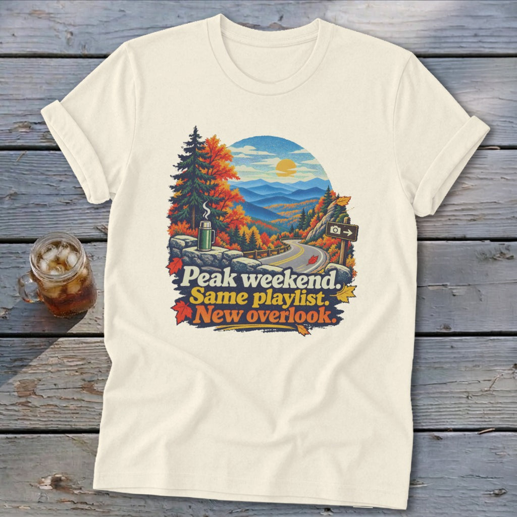 Cream t-shirt with graphic of scenic overlook, autumn trees, and text "Peak weekend. Same playlist. New overlook."