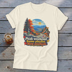 Cream t-shirt with graphic of scenic overlook, autumn trees, and text "Peak weekend. Same playlist. New overlook."