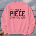 Pink sweatshirt with distressed black and red text reading "JUST A PIECE DOWN THE ROAD".