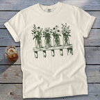 An off-white t-shirt featuring a green graphic of four mason jars filled with wildflowers on a shelf.