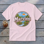 Pink t-shirt with a circular graphic of mountains, river, trees, and deer, reading "Maryland".