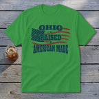 A green short-sleeve t-shirt with a distressed graphic featuring red and blue American flags and the text OHIO RAISED AMERICAN MADE.