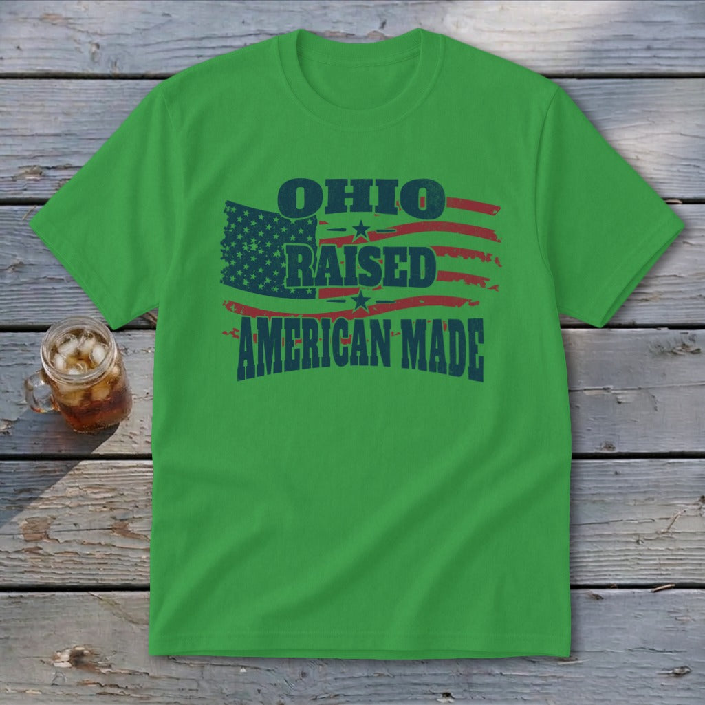 A green short-sleeve t-shirt with a distressed graphic featuring red and blue American flags and the text OHIO RAISED AMERICAN MADE.