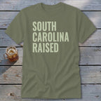 Olive green t-shirt with "SOUTH CAROLINA RAISED" text in light cream.