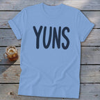 Light blue t-shirt with "YUNS" printed in navy blue, next to a glass of iced tea.