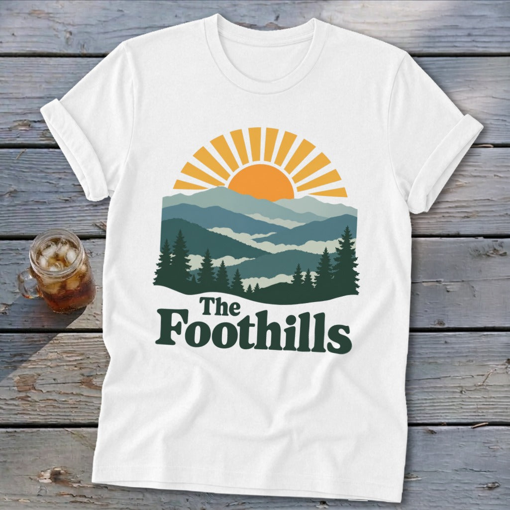 White t-shirt with a mountain and sun graphic and "The Foothills" text.