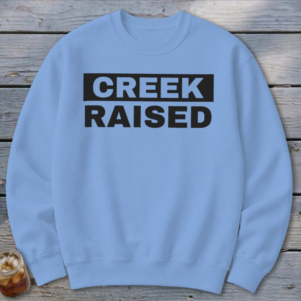 Light blue crewneck sweatshirt with "CREEK RAISED" text in black block letters.