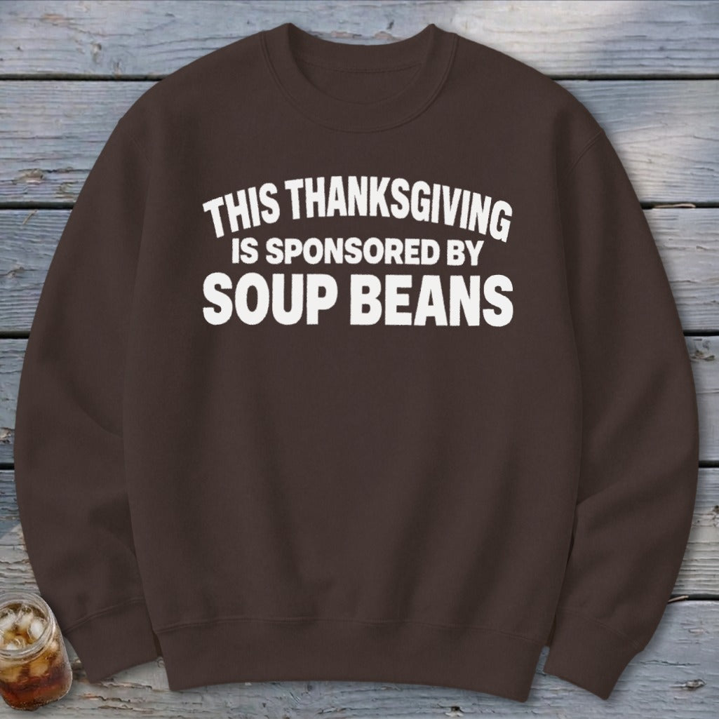 A brown crewneck sweatshirt featuring white text that reads THIS THANKSGIVING IS SPONSORED BY SOUP BEANS.
