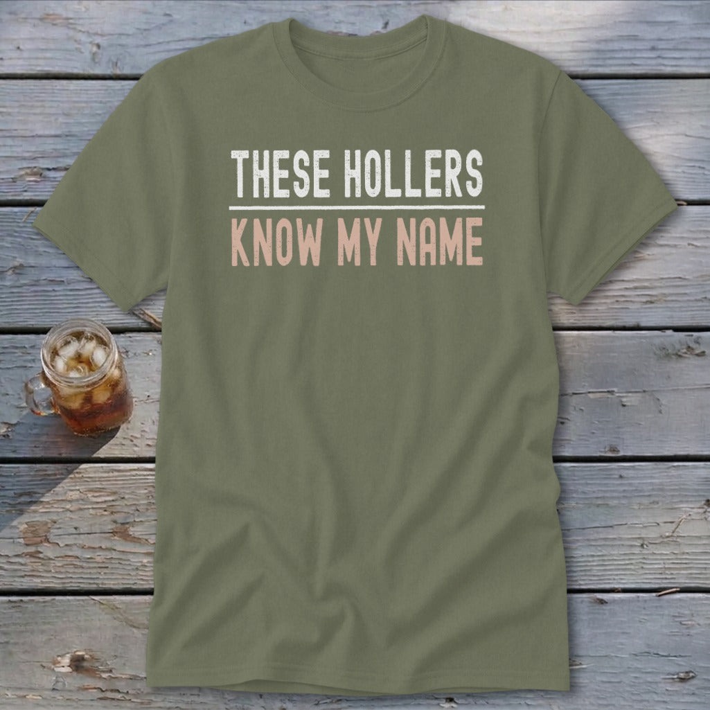 Olive green t-shirt with white and pink text reading "THESE HOLLERS KNOW MY NAME".