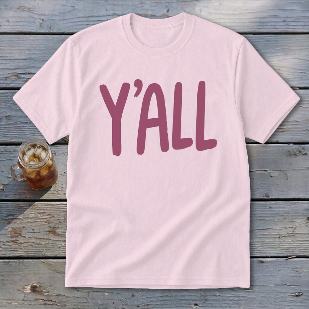Pink t-shirt with large maroon "Y'ALL" text, set on a wooden surface.