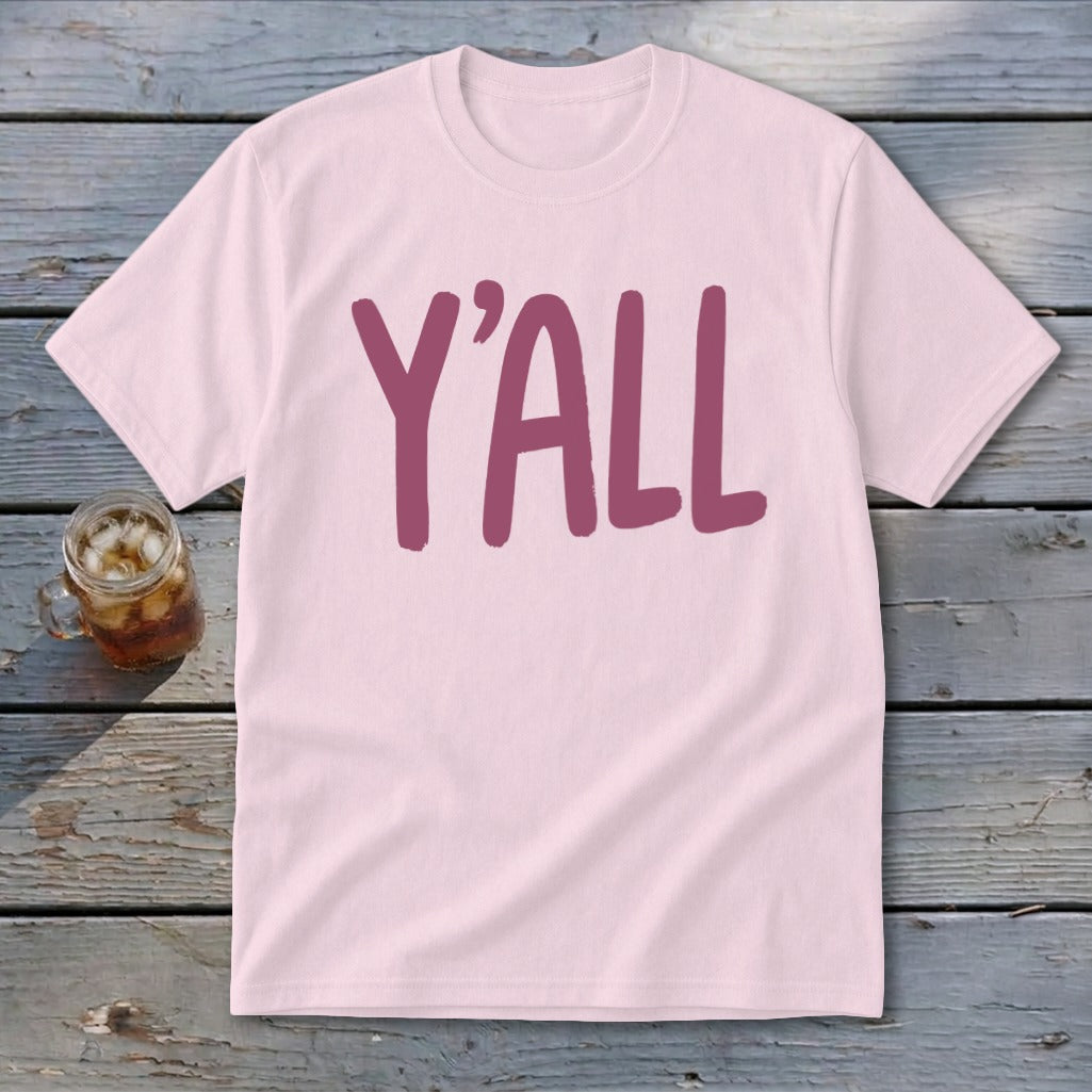Pink t-shirt with large maroon "Y'ALL" text, set on a wooden surface.