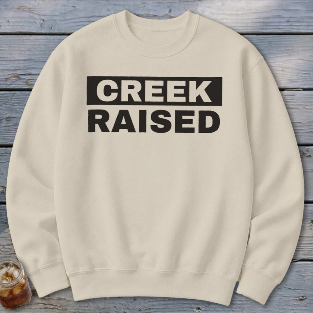 Cream sweatshirt with "CREEK RAISED" text in black rectangular boxes.