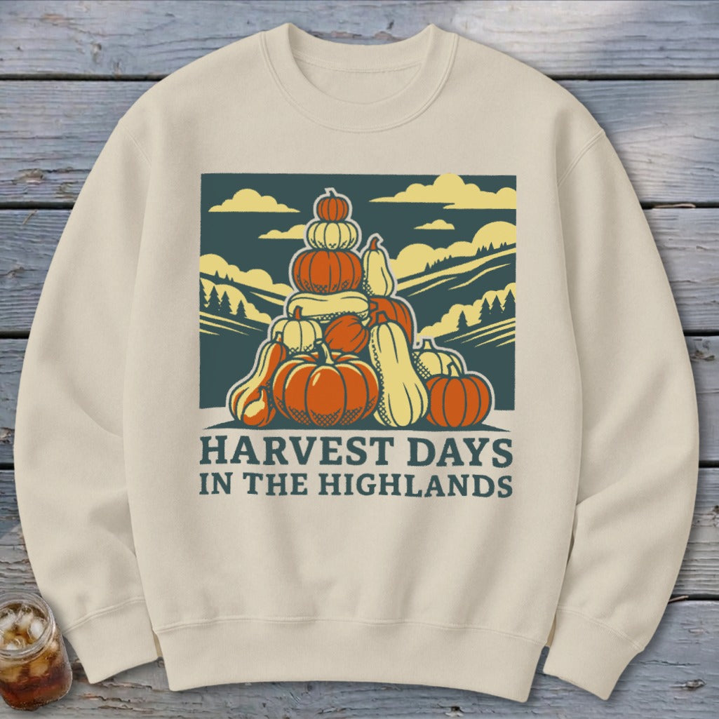 A cream-colored crewneck sweatshirt featuring a graphic of a large stack of pumpkins and gourds against a mountainous landscape with the text HARVEST DAYS IN THE HIGHLANDS.