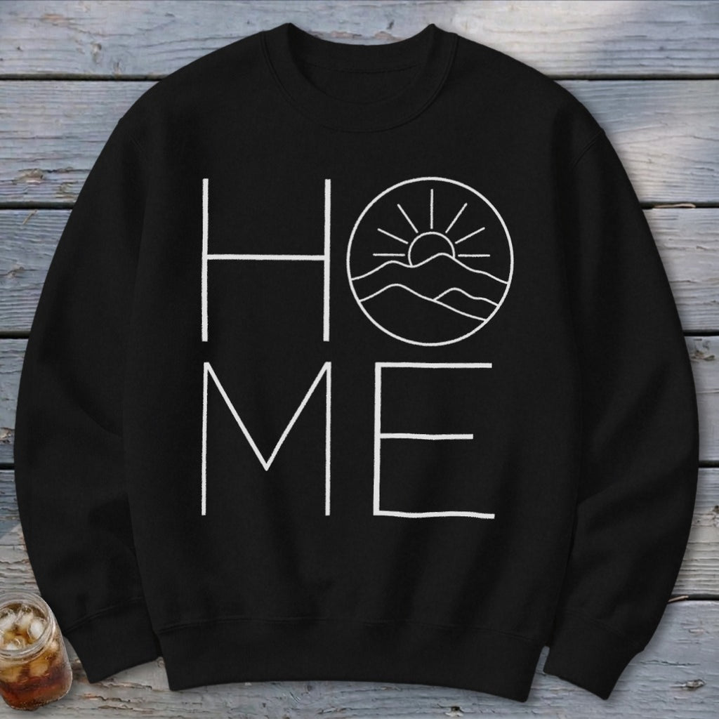A black crewneck sweatshirt features white text spelling HOME, with a mountain and sun graphic inside the O.