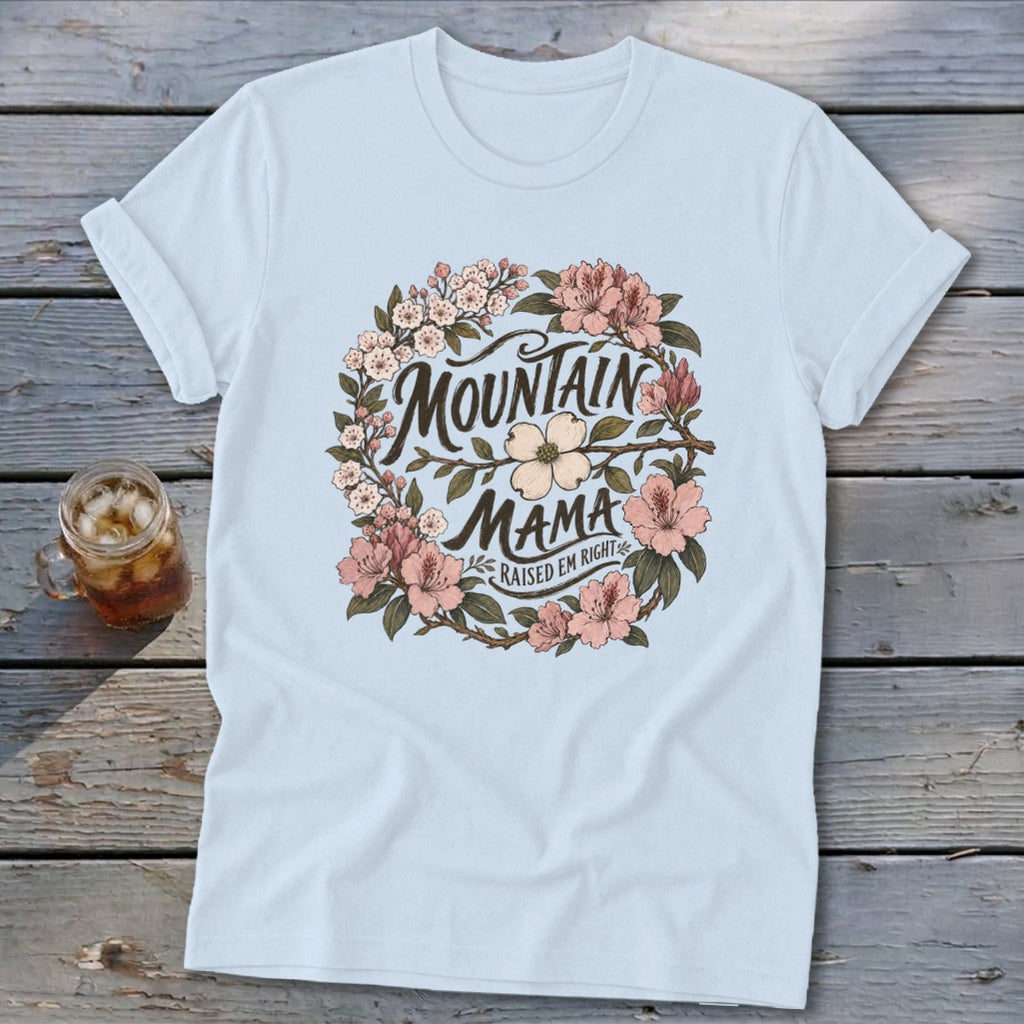 Light blue t-shirt with "Mountain Mama Raised Em Right" text within a floral wreath.
